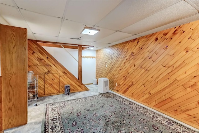 basement featuring a paneled ceiling and wooden walls