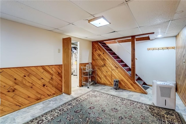 basement with a drop ceiling and wooden walls