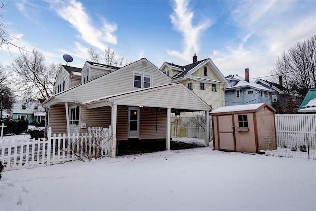 snow covered back of property featuring a storage shed