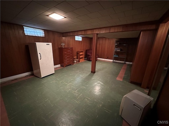 basement featuring refrigerator and wood walls