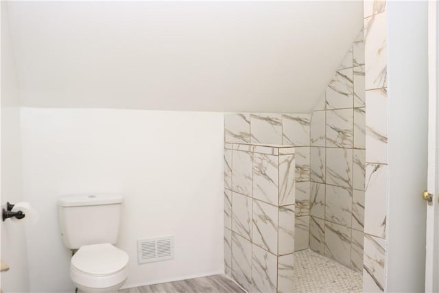 bathroom featuring toilet, vaulted ceiling, and tiled shower