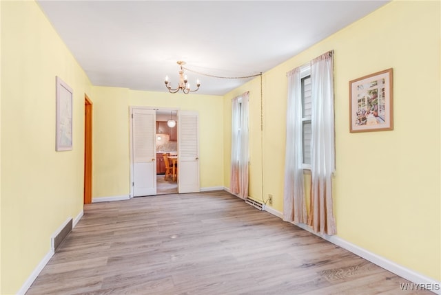 spare room with an inviting chandelier and light hardwood / wood-style flooring