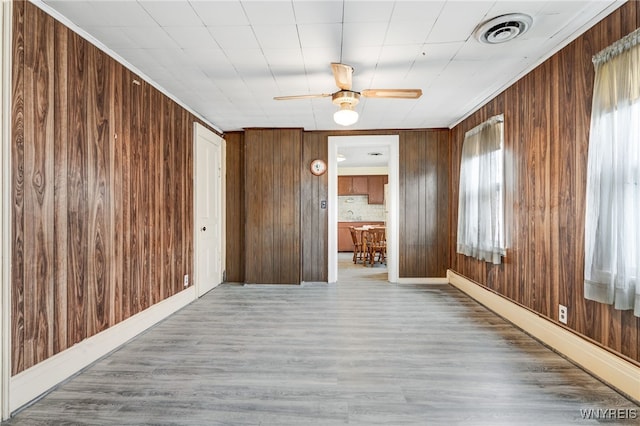 unfurnished room featuring ceiling fan, a baseboard heating unit, wooden walls, and wood-type flooring