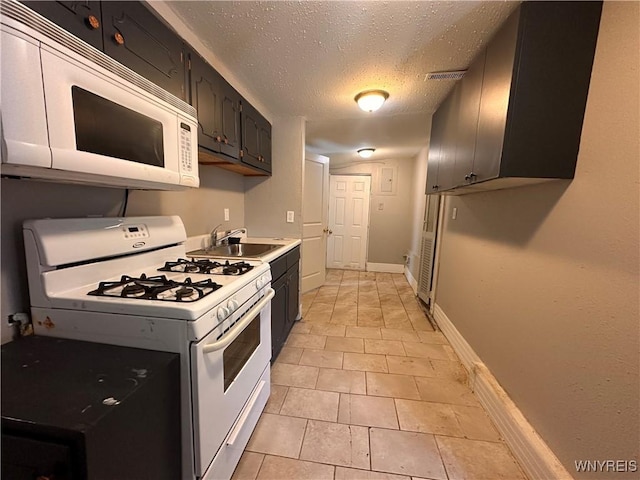 kitchen featuring sink, white appliances, light tile patterned floors, and a textured ceiling