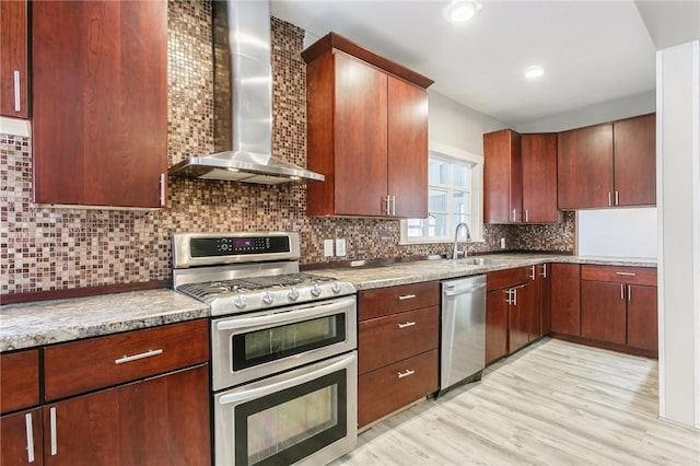 kitchen featuring appliances with stainless steel finishes, tasteful backsplash, light wood-type flooring, wall chimney range hood, and sink