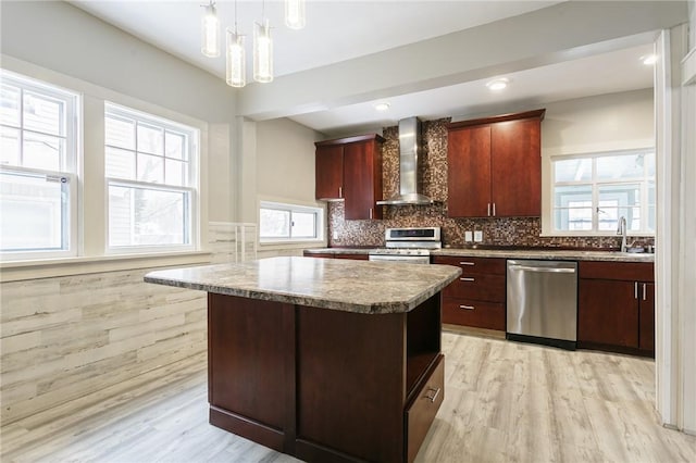 kitchen with pendant lighting, appliances with stainless steel finishes, a center island, wall chimney range hood, and sink