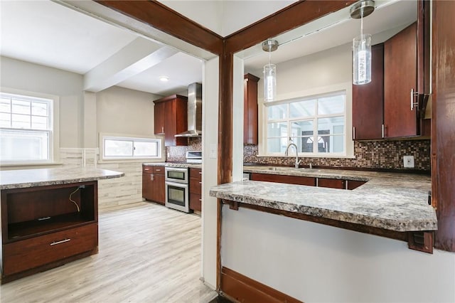 kitchen featuring plenty of natural light, range with two ovens, hanging light fixtures, wall chimney exhaust hood, and sink