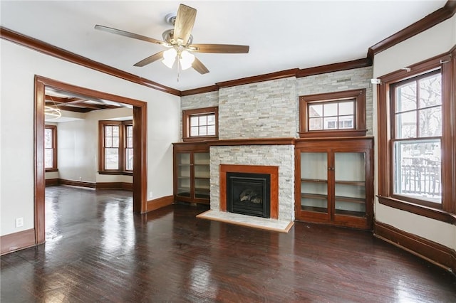 unfurnished living room with ceiling fan, dark hardwood / wood-style flooring, ornamental molding, and a stone fireplace