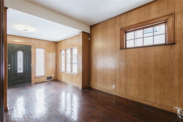 foyer with dark wood-type flooring, a healthy amount of sunlight, and wooden walls