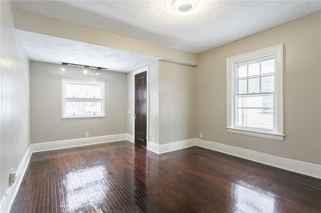 empty room with dark wood-type flooring, a textured ceiling, and rail lighting