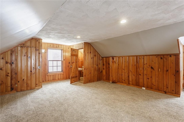 bonus room featuring carpet floors, a textured ceiling, wood walls, and lofted ceiling