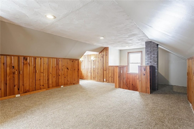 bonus room featuring a textured ceiling, vaulted ceiling, carpet flooring, and wooden walls