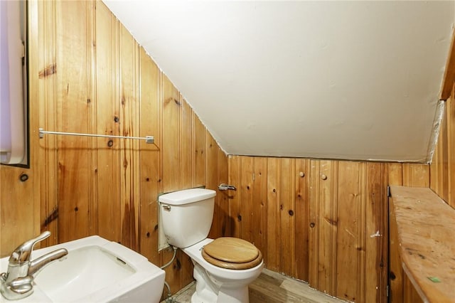 bathroom with hardwood / wood-style floors, lofted ceiling, sink, toilet, and wood walls