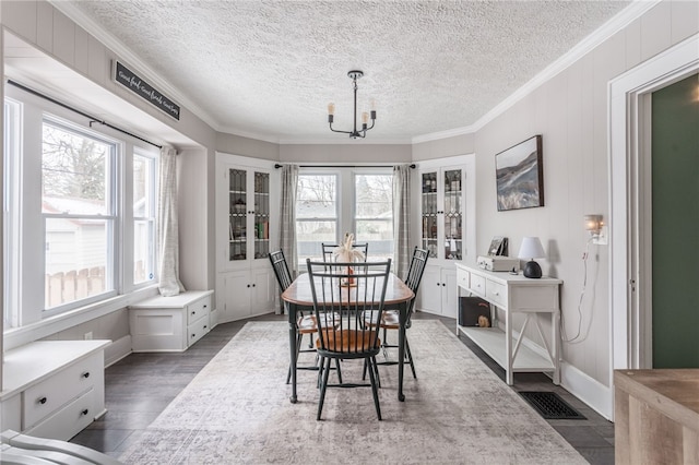 dining room featuring a textured ceiling, dark hardwood / wood-style floors, crown molding, and a chandelier