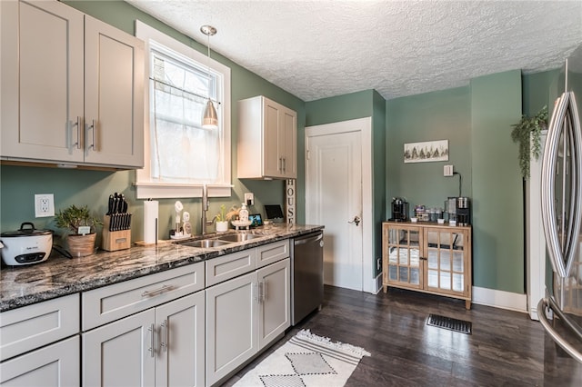 kitchen with a textured ceiling, appliances with stainless steel finishes, white cabinetry, dark stone countertops, and sink