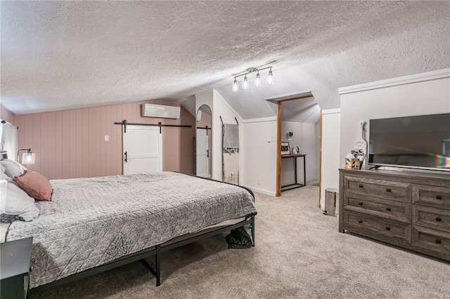 carpeted bedroom featuring a textured ceiling, wooden walls, vaulted ceiling, a barn door, and a wall mounted air conditioner