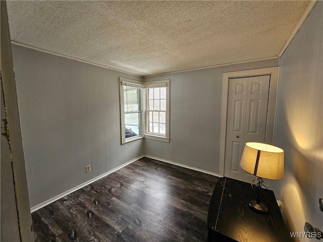 empty room with a textured ceiling, dark hardwood / wood-style flooring, and wooden walls