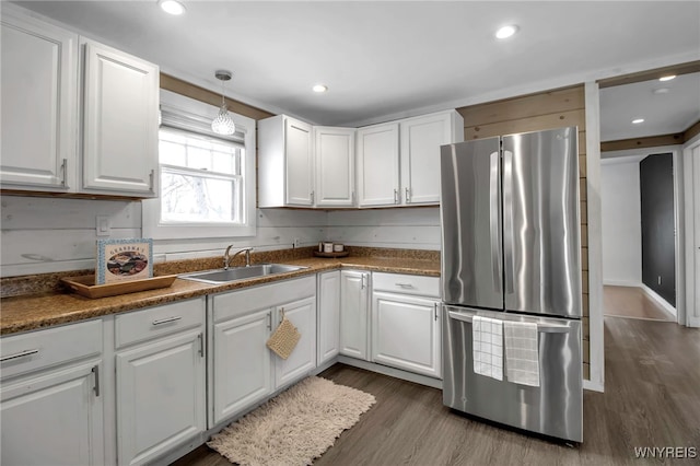 kitchen featuring white cabinetry, stainless steel fridge, dark wood-type flooring, hanging light fixtures, and sink