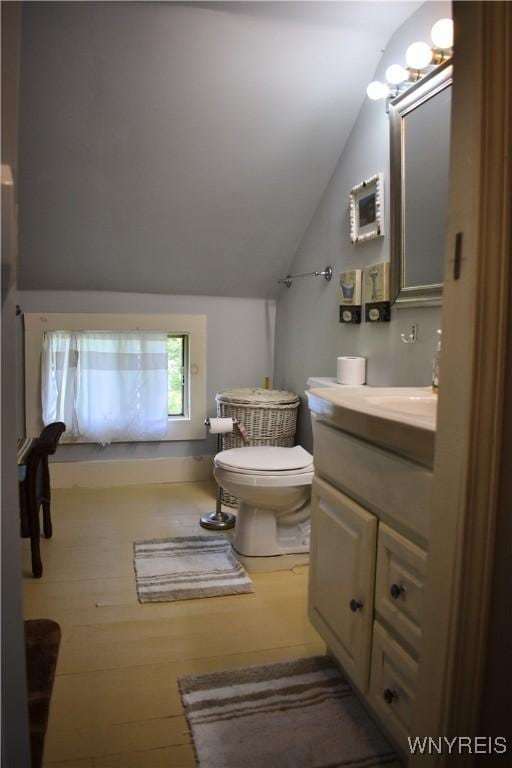 bathroom featuring toilet, vanity, wood-type flooring, and lofted ceiling