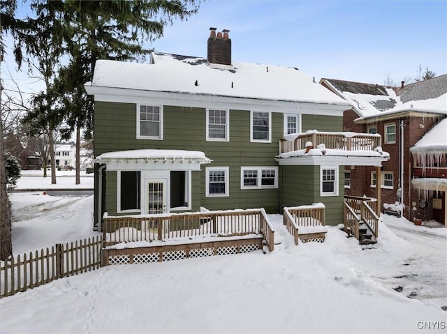 snow covered back of property with a wooden deck