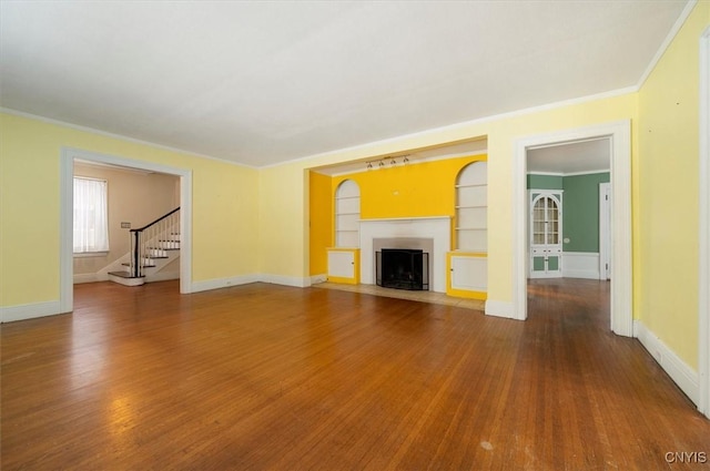 unfurnished living room featuring built in shelves, crown molding, and hardwood / wood-style floors