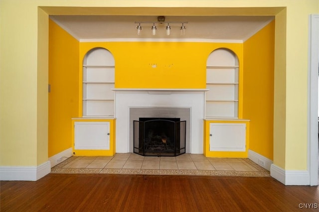 unfurnished living room with wood-type flooring, built in features, and crown molding