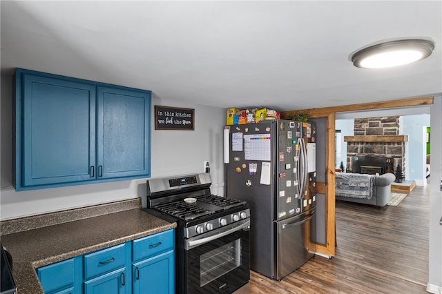 kitchen featuring blue cabinets, dark hardwood / wood-style flooring, appliances with stainless steel finishes, and a fireplace