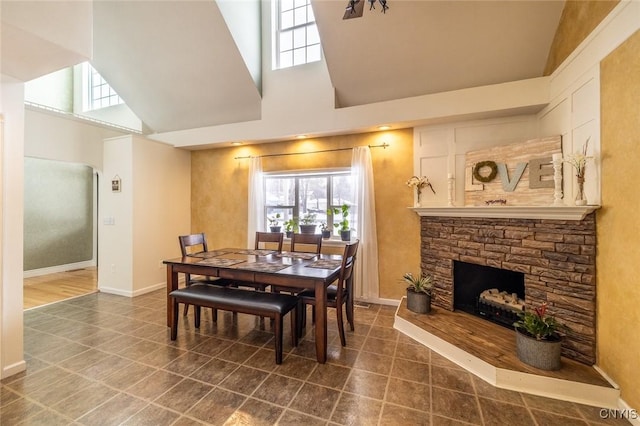 tiled dining room featuring a high ceiling and a stone fireplace