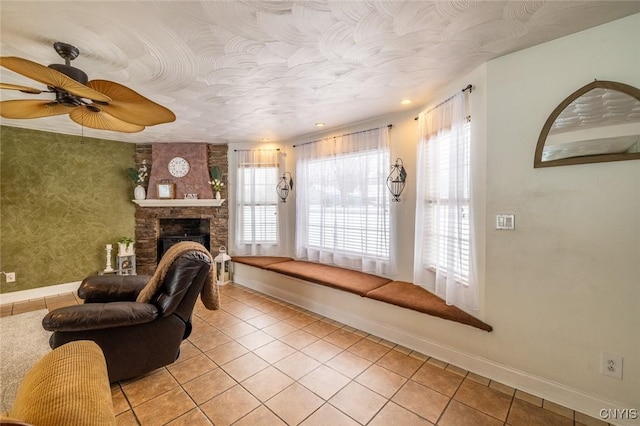 tiled living room with ceiling fan and a fireplace