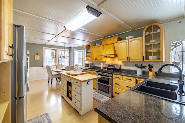 kitchen with appliances with stainless steel finishes, a center island, custom exhaust hood, sink, and butcher block countertops