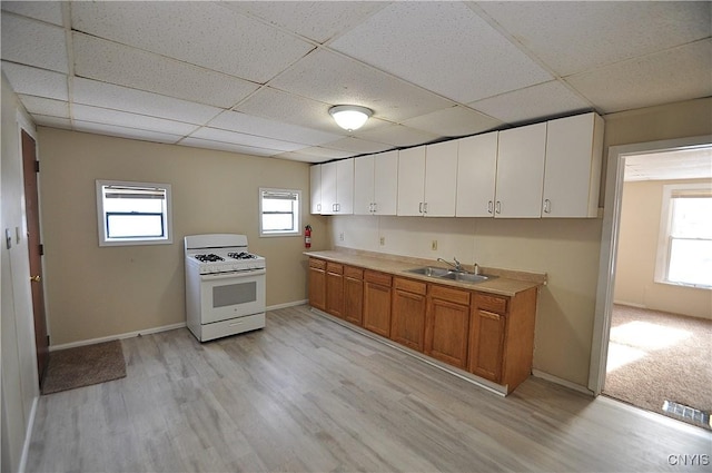 kitchen featuring white range with gas stovetop, white cabinetry, light hardwood / wood-style flooring, and a drop ceiling