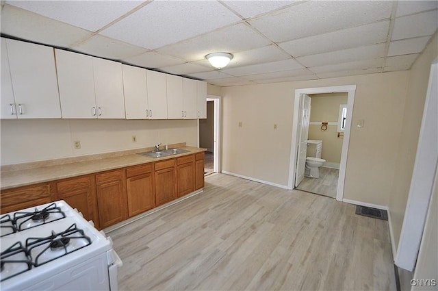 kitchen with white cabinetry, white range with gas stovetop, light wood-type flooring, a drop ceiling, and sink