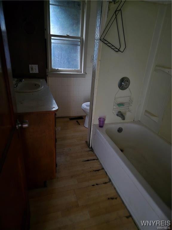 full bathroom featuring toilet, hardwood / wood-style flooring, shower / washtub combination, tile walls, and vanity