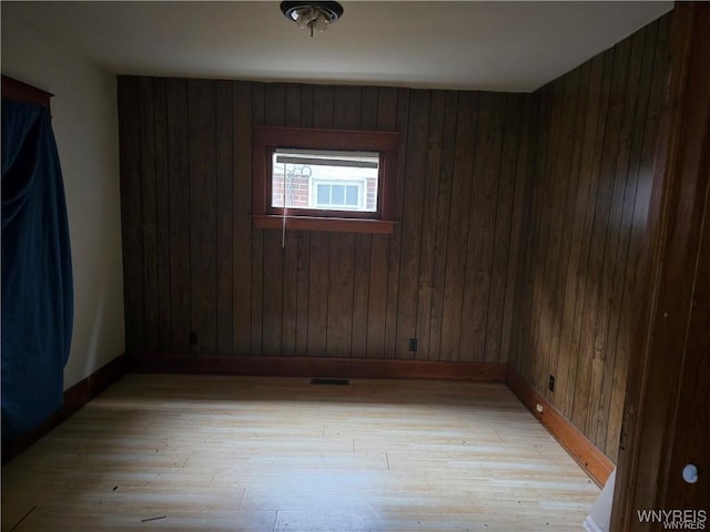 spare room featuring light hardwood / wood-style floors and wooden walls