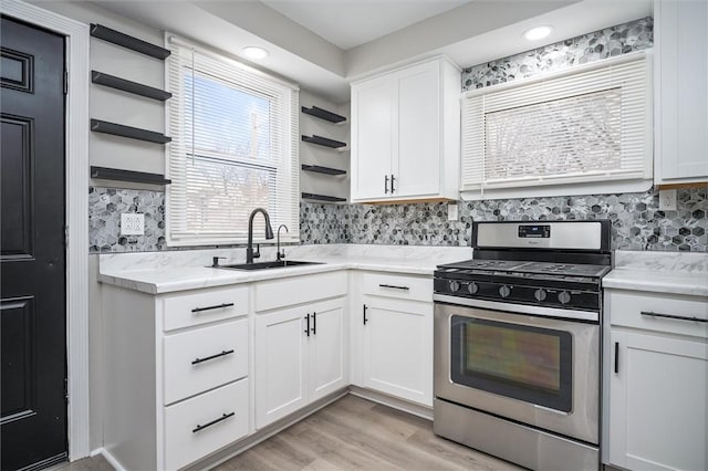 kitchen with white cabinetry, gas stove, light wood-type flooring, light stone countertops, and sink