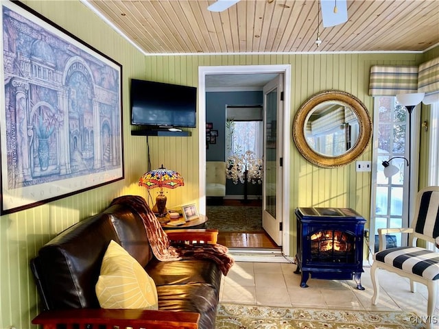 sitting room with light tile patterned floors, ceiling fan, ornamental molding, wooden ceiling, and a wood stove