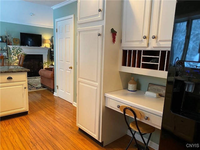 kitchen featuring white cabinetry, built in desk, black refrigerator with ice dispenser, and light hardwood / wood-style flooring