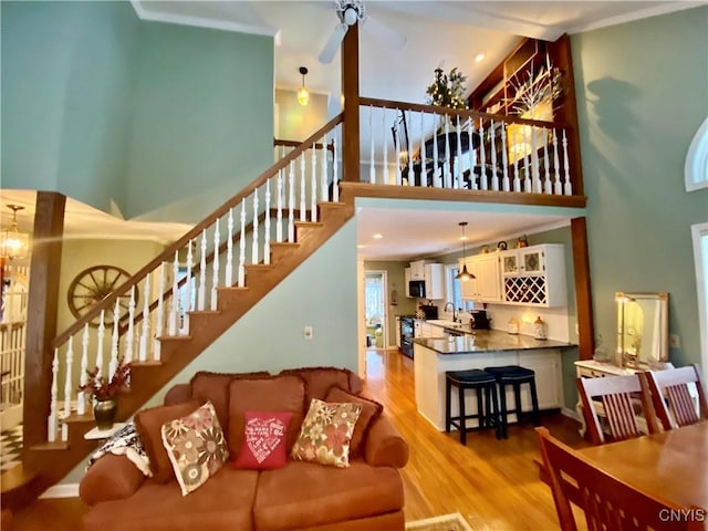 living room with sink, a high ceiling, ceiling fan, light hardwood / wood-style floors, and crown molding