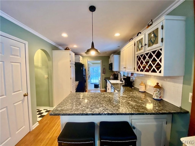 kitchen with hanging light fixtures, kitchen peninsula, white cabinets, and black fridge