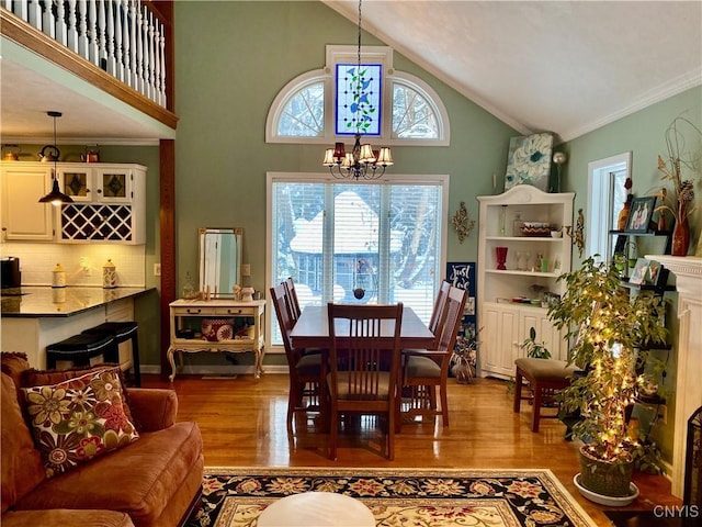 dining space with ornamental molding, lofted ceiling, a chandelier, and light hardwood / wood-style flooring