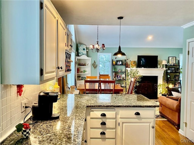 kitchen featuring white cabinetry, hanging light fixtures, light stone counters, a notable chandelier, and decorative backsplash