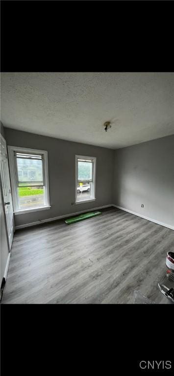 unfurnished room featuring a textured ceiling, baseboards, and wood finished floors