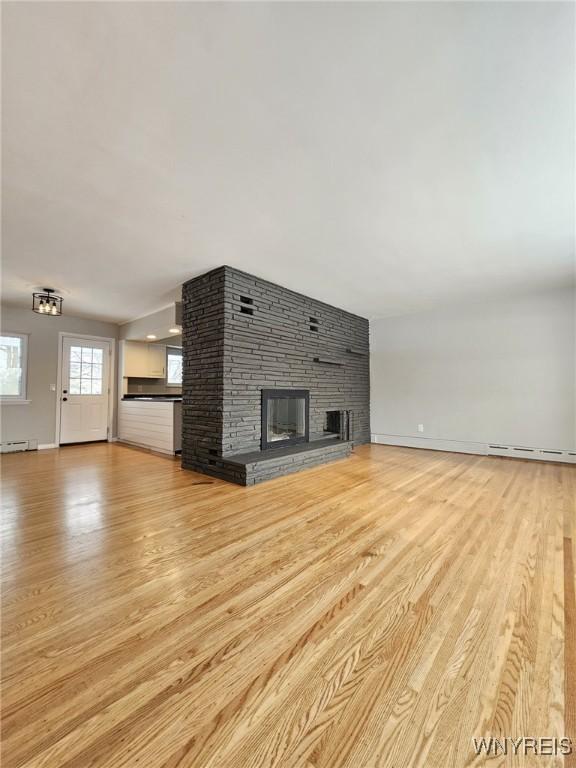 unfurnished living room featuring light hardwood / wood-style floors, a baseboard heating unit, and a fireplace