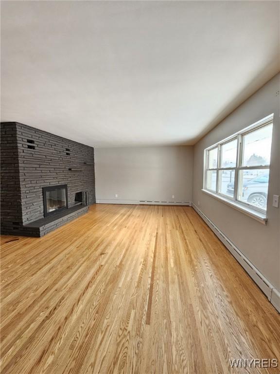 unfurnished living room with baseboard heating, a fireplace, and light hardwood / wood-style flooring