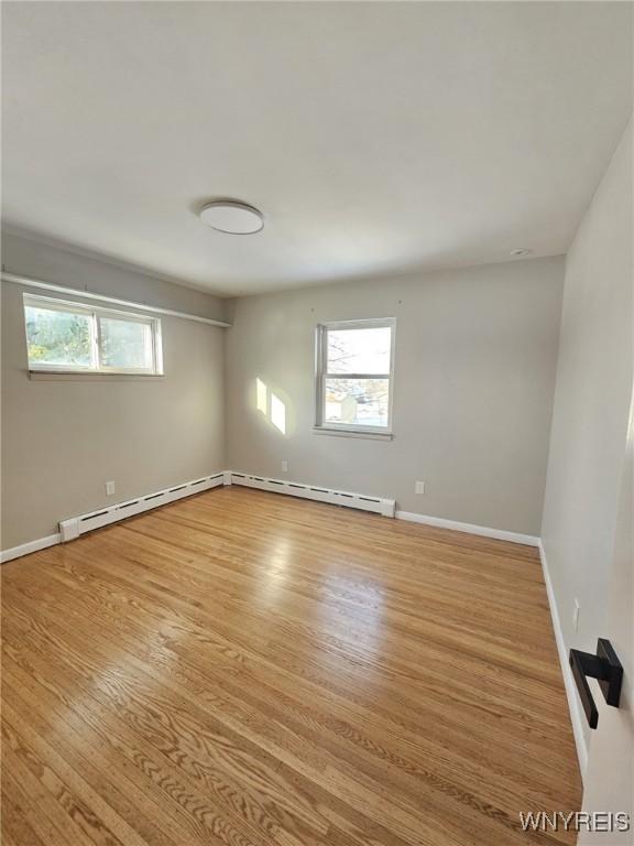 spare room with a baseboard radiator, a wealth of natural light, and light wood-type flooring