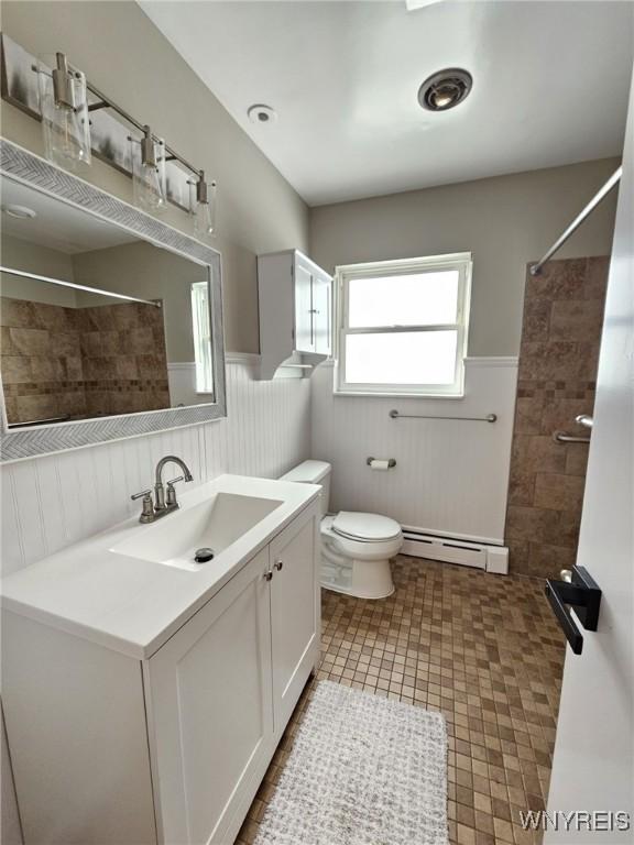 bathroom featuring toilet, tiled shower, vanity, and a baseboard radiator