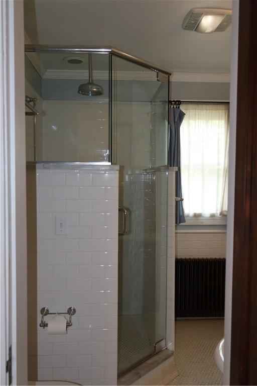 bathroom with radiator, a shower with door, and ornamental molding