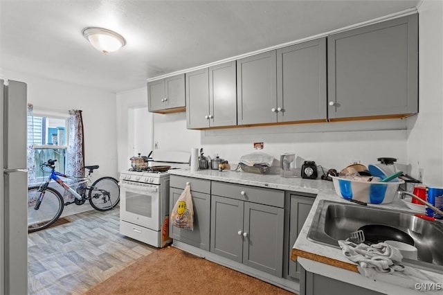 kitchen with white range with gas cooktop, light hardwood / wood-style floors, sink, refrigerator, and gray cabinetry