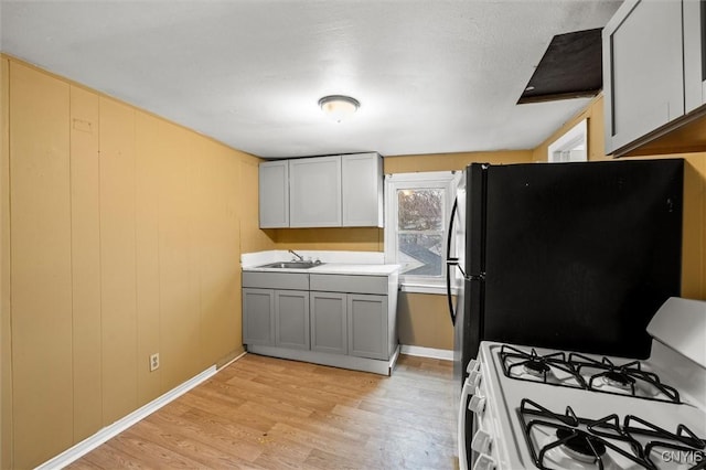 kitchen featuring gray cabinetry, black fridge, light wood-type flooring, white gas range, and sink