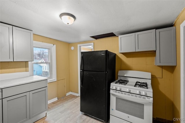 kitchen featuring black refrigerator, gray cabinets, light wood-type flooring, a textured ceiling, and white gas range